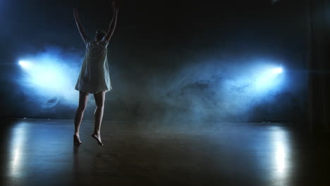 Modern-dance-woman-in-a-white-dress-dances-a-modern-ballet-jumps-makes-rotation-on-the-stage-with-smoke-in-the-blue-spotlights